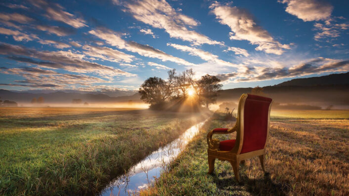 Ein roter Stuhl steht bei Sonnenaufgang mitten auf einem Feld.